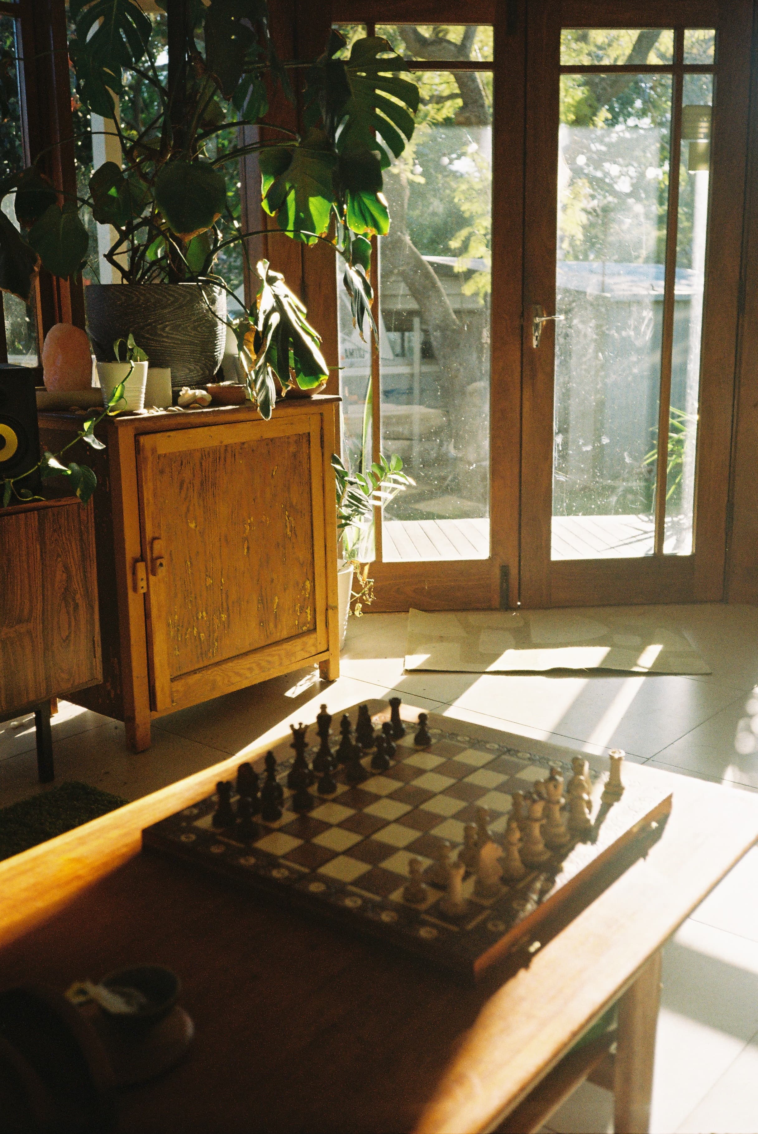 A chess game mid-play on a wooden table, afternoon light through open doors