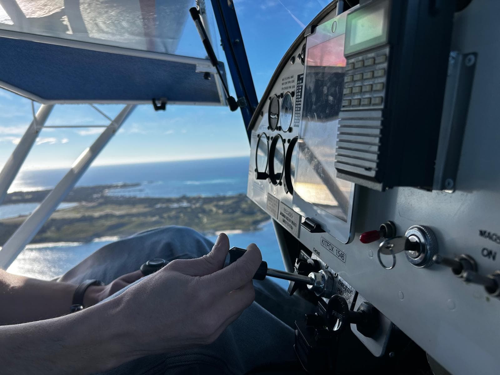 Hand on the throttle in the cockpit of a Kitfox light aircraft, coastline below
